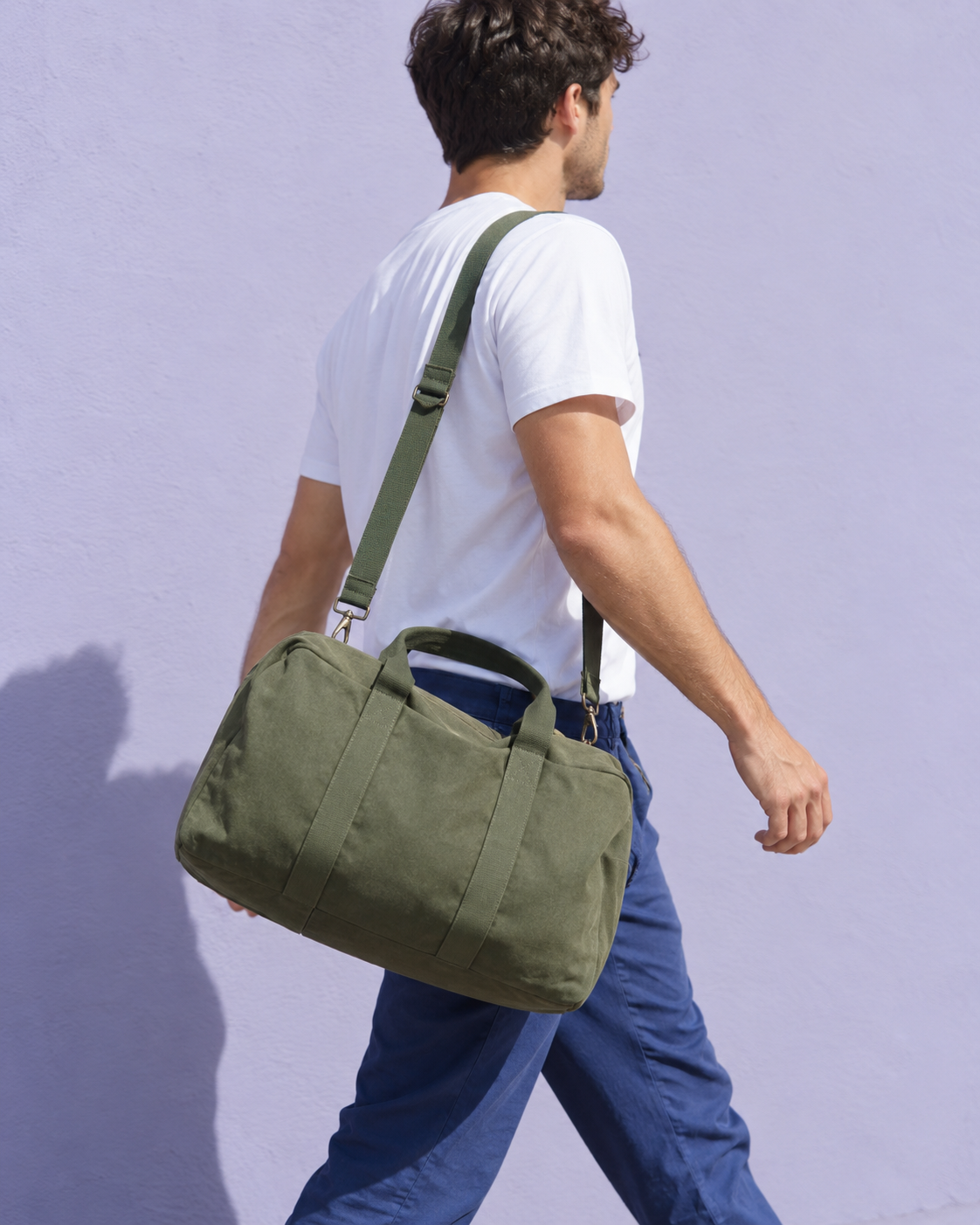 A person carrying a green weekender beside a clean lavender wall