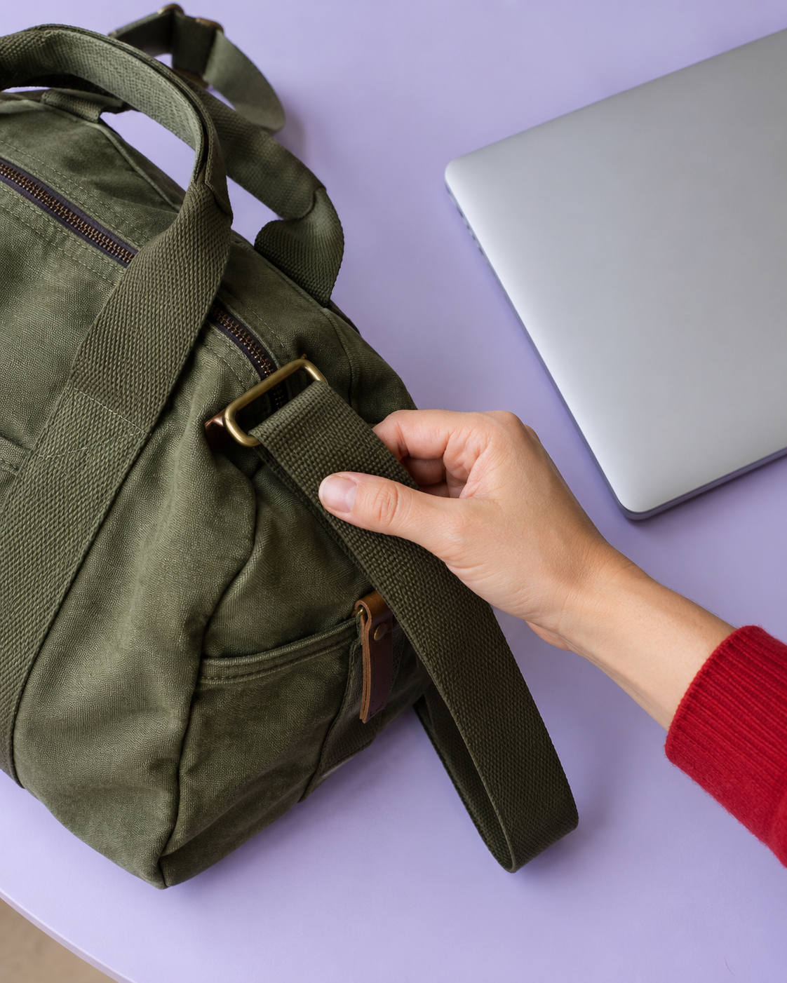 A hand checking a weekender strap beside a laptop on a lilac table